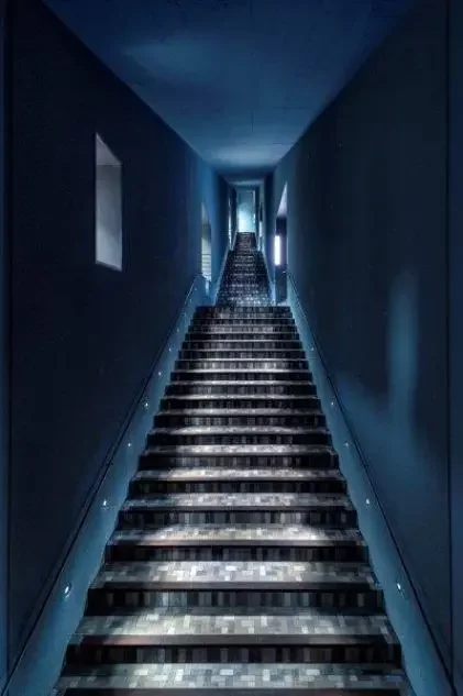 Blau gestrichenes Treppenhaus mit Treppe, die sich nach oben hin stark verjüngt